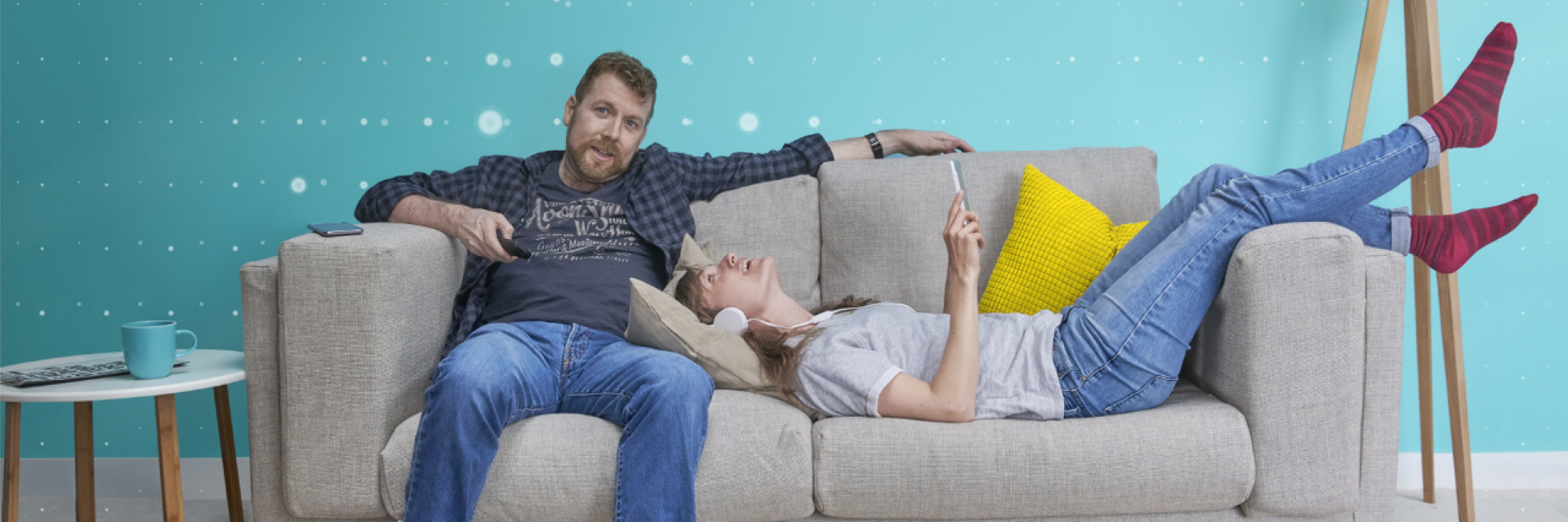 A young couple relaxing on a sofa, the man watching Apple TV, the woman using her phone
