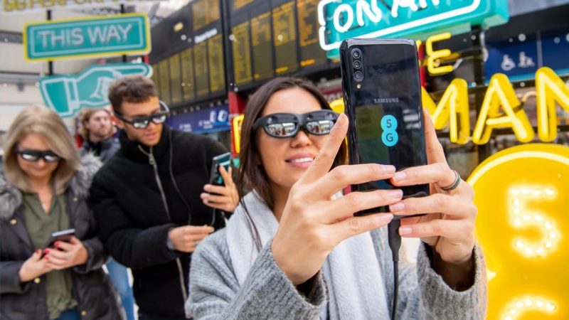 woman holding up her phone with 5G on the back and wearing VR glasses