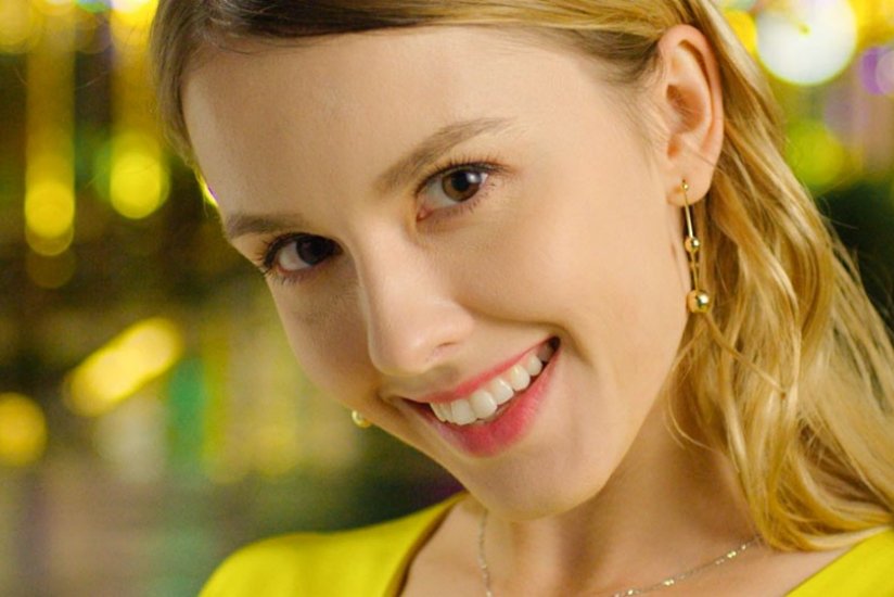 A portrait of a young woman wearing a yellow top and gold jewellery on a yellow-lit background